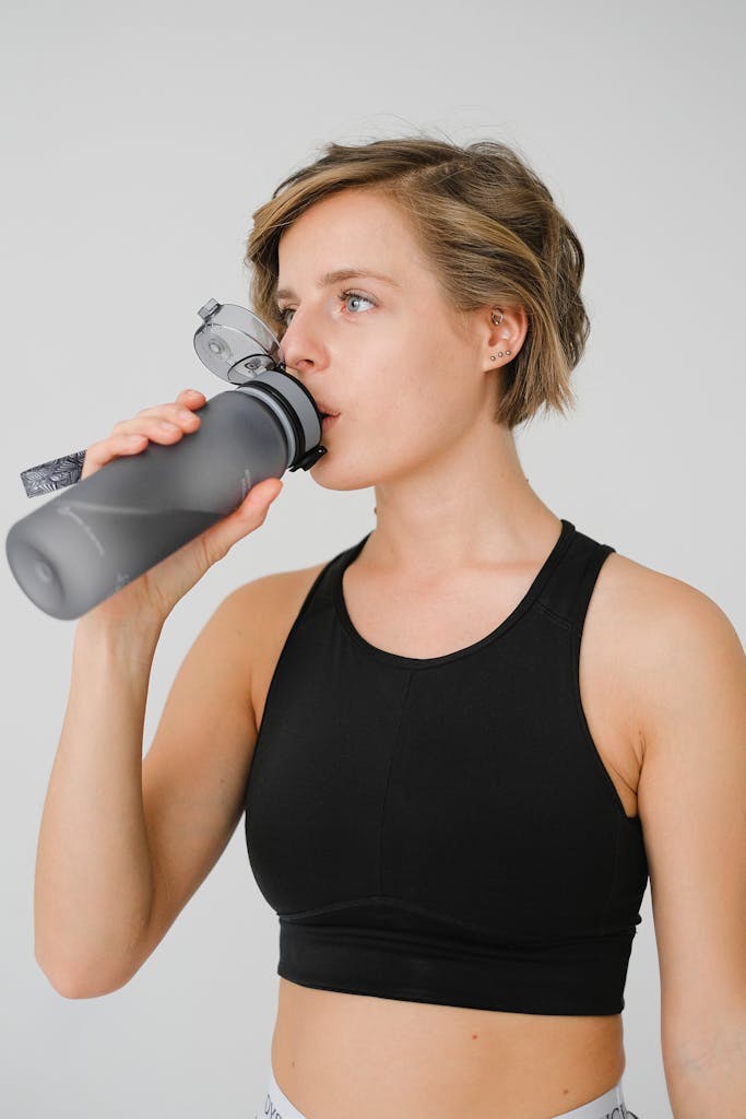 Young woman in athletic wear sipping water from a reusable bottle, promoting hydration and fitness.