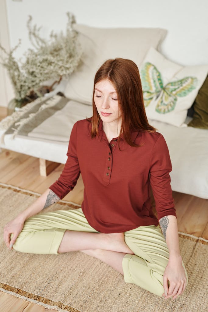 Young woman practicing meditation indoors, sitting cross-legged on a yoga mat.