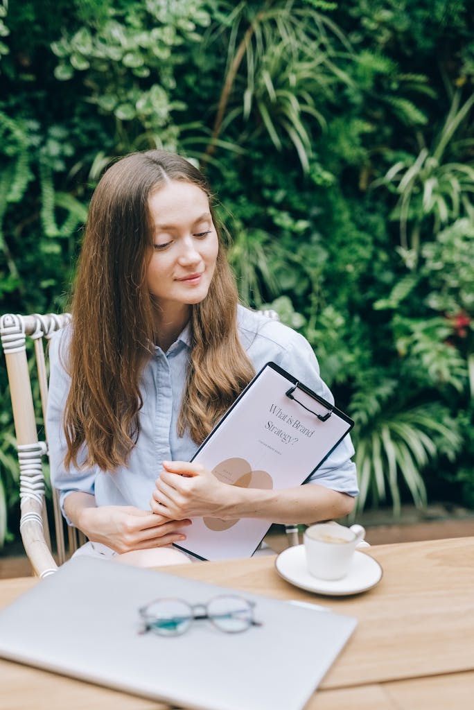 Young woman with clipboard enjoys coffee break in lush garden setting, symbolizing work-life balance.