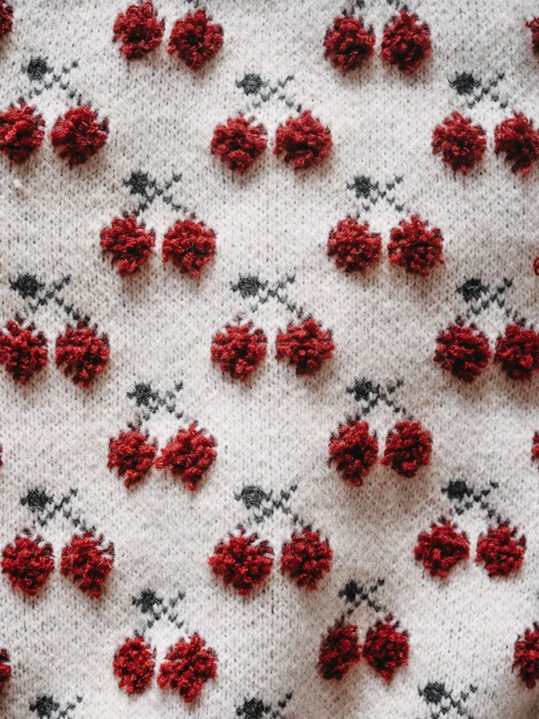 Close-up of embroidered cherry pattern on knitted white fabric for fashion and design.