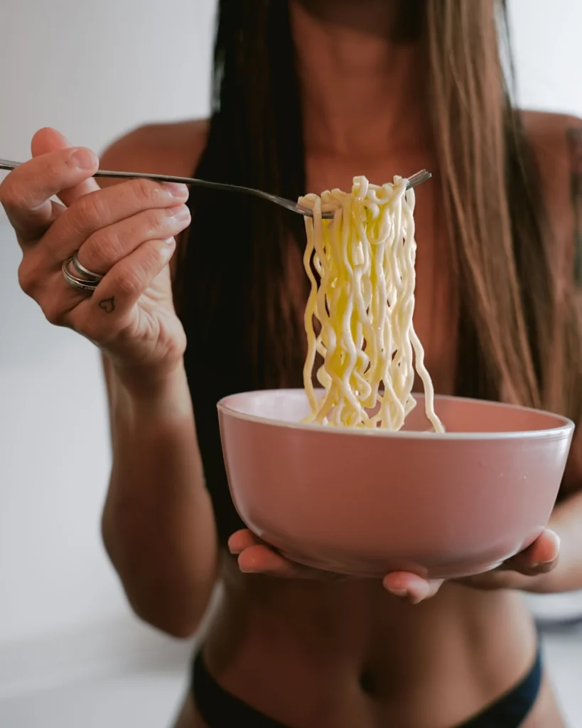 Woman eating noodles from a pink bowl.