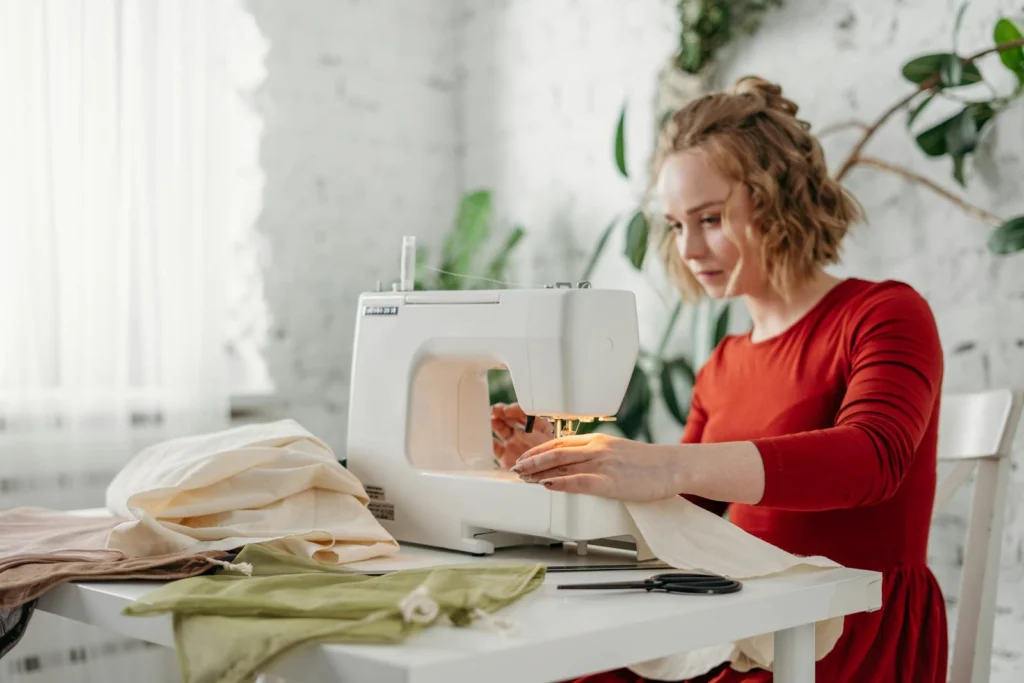 A woman in a red dress using a sewing machine at home, creating a handmade garment.