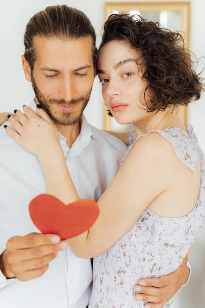 A loving couple embraces while holding a heart-shaped cutout, creating a warm and affectionate scene.