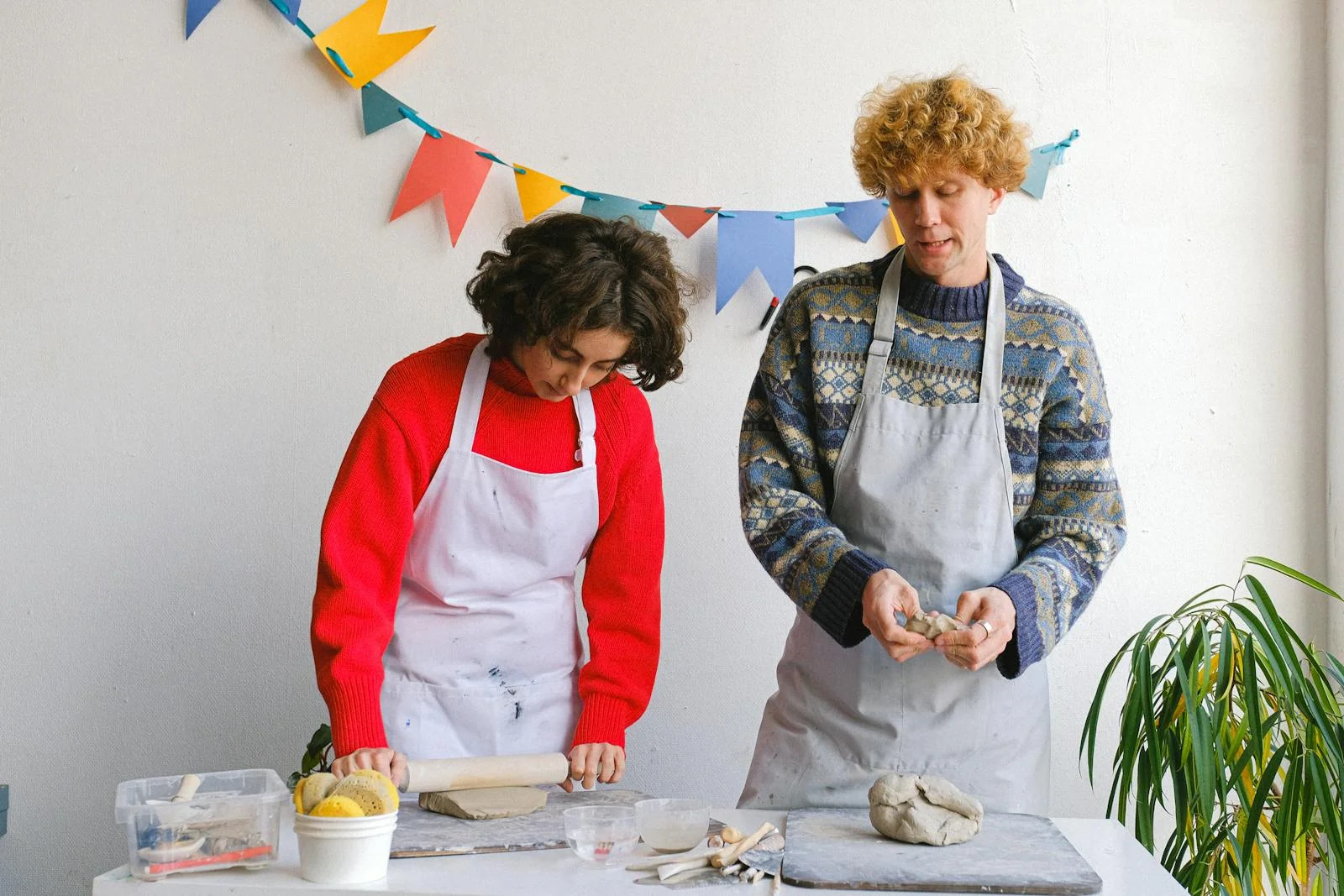 Two artisans wearing aprons crafting pottery in a bright indoor studio.