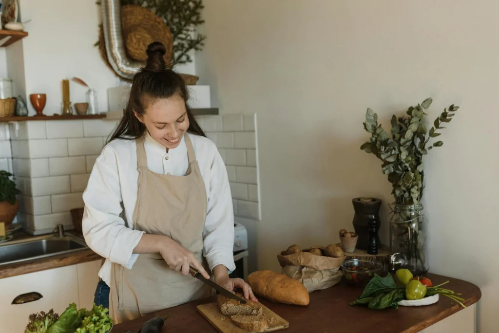 A cheerful woman slices bread in a warm, inviting kitchen. Perfect for lifestyle and culinary themes.