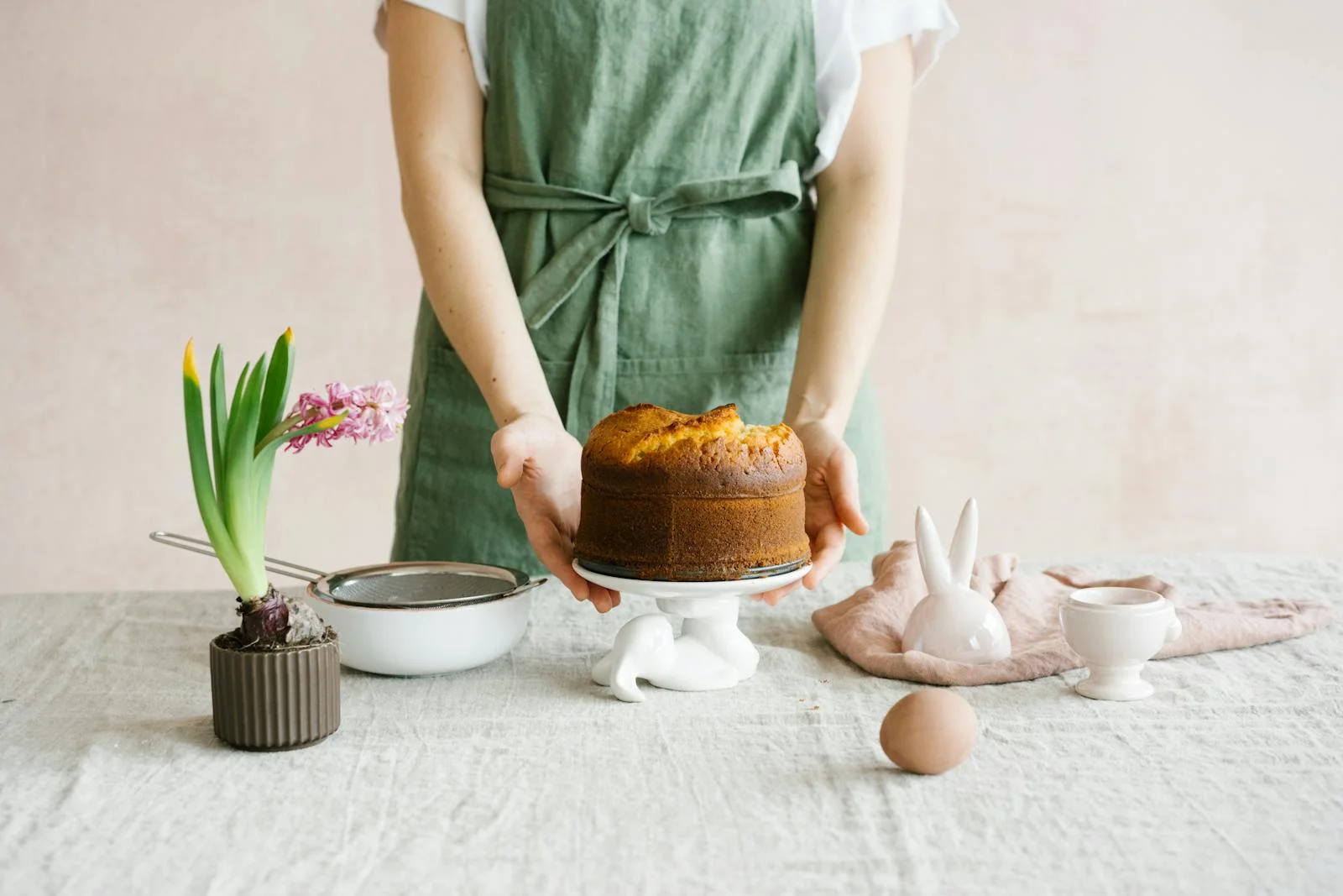 A person preparing an Easter cake with bunny decorations and spring flowers on a table.