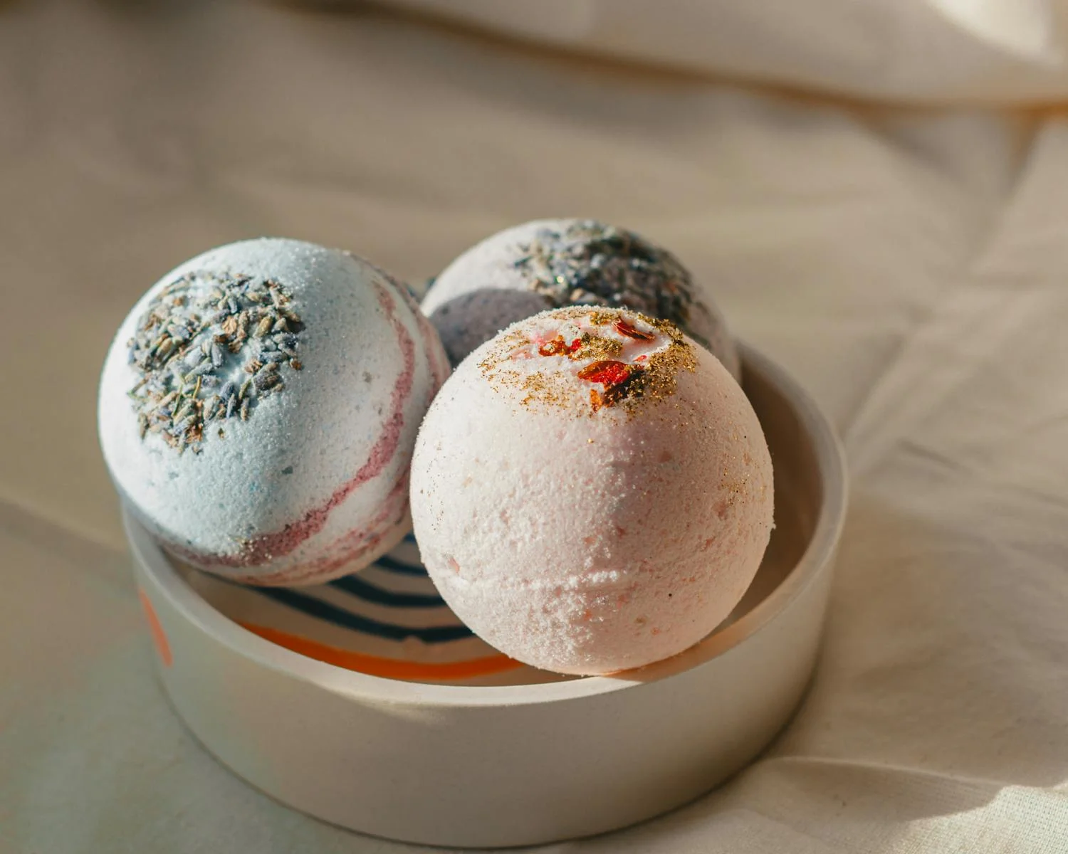 Three pastel bath bombs arranged in a ceramic dish for a spa-themed setting.
