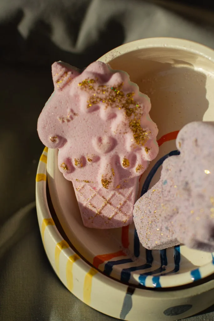 A pink unicorn-shaped bath bomb with gold glitter sits in a colorful bowl, ideal for spa and relaxation themes.