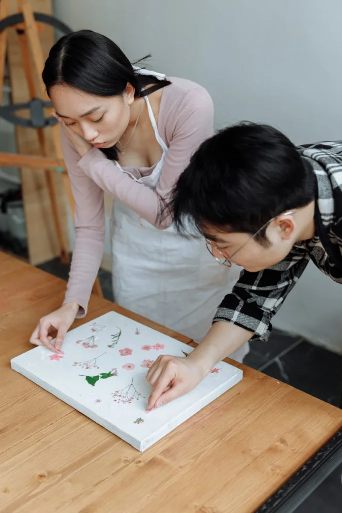 Asian man and woman collaborating on floral art decoration indoors. Creative teamwork and focus.