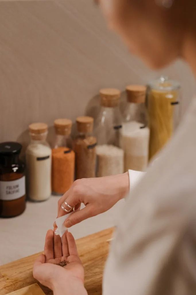 A woman prepares a meal by pinching spices onto a wooden cutting board in a kitchen setting.