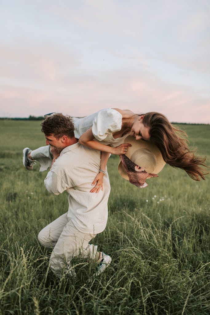 A couple enjoys a playful moment in a scenic grassy field during sunset, filled with love and joy.