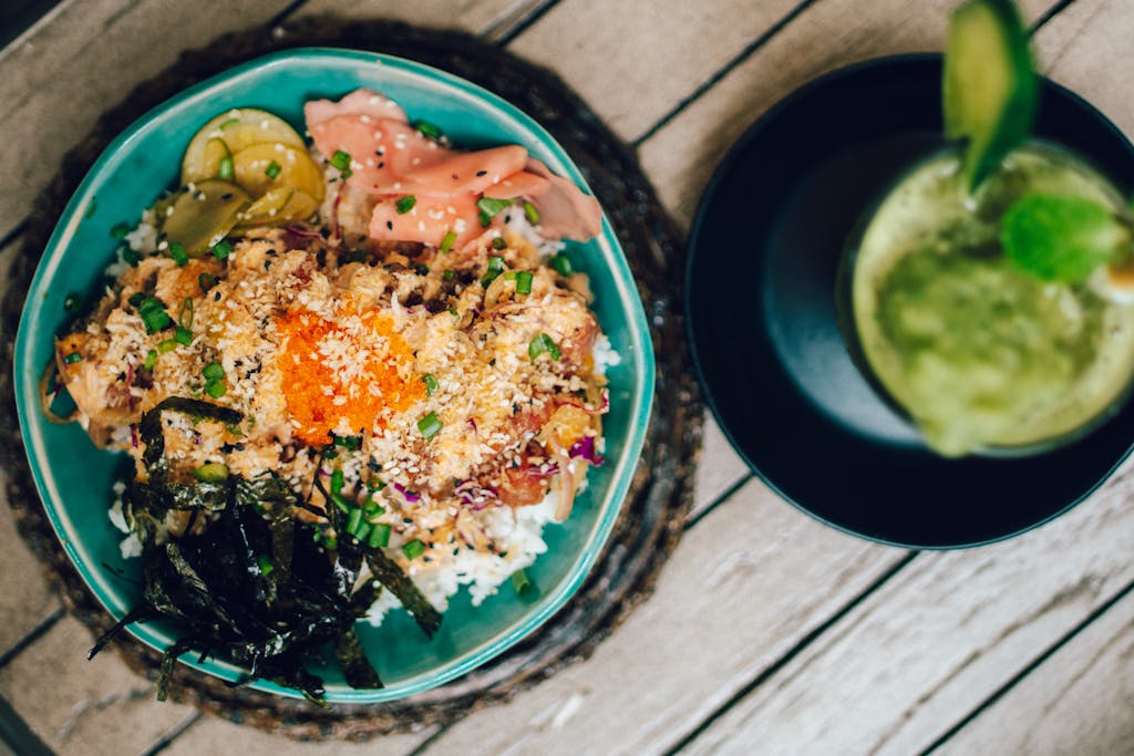 A delicious and colorful poke bowl dish featuring fresh seafood, vegetables, and rice, served with a green smoothie.