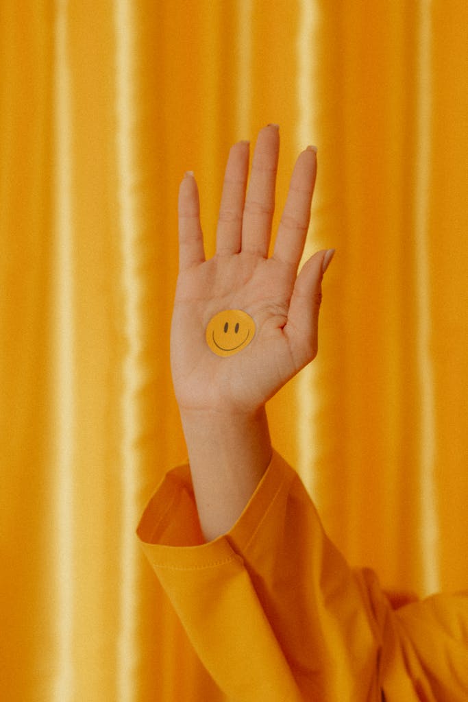 A hand featuring a smiley sticker stands out against a vibrant yellow backdrop, conveying positivity.