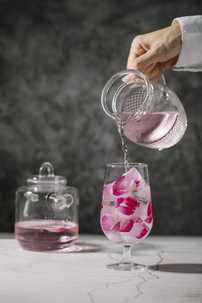 A hand pours rose-infused water with petals into a glass, highlighting refreshment.