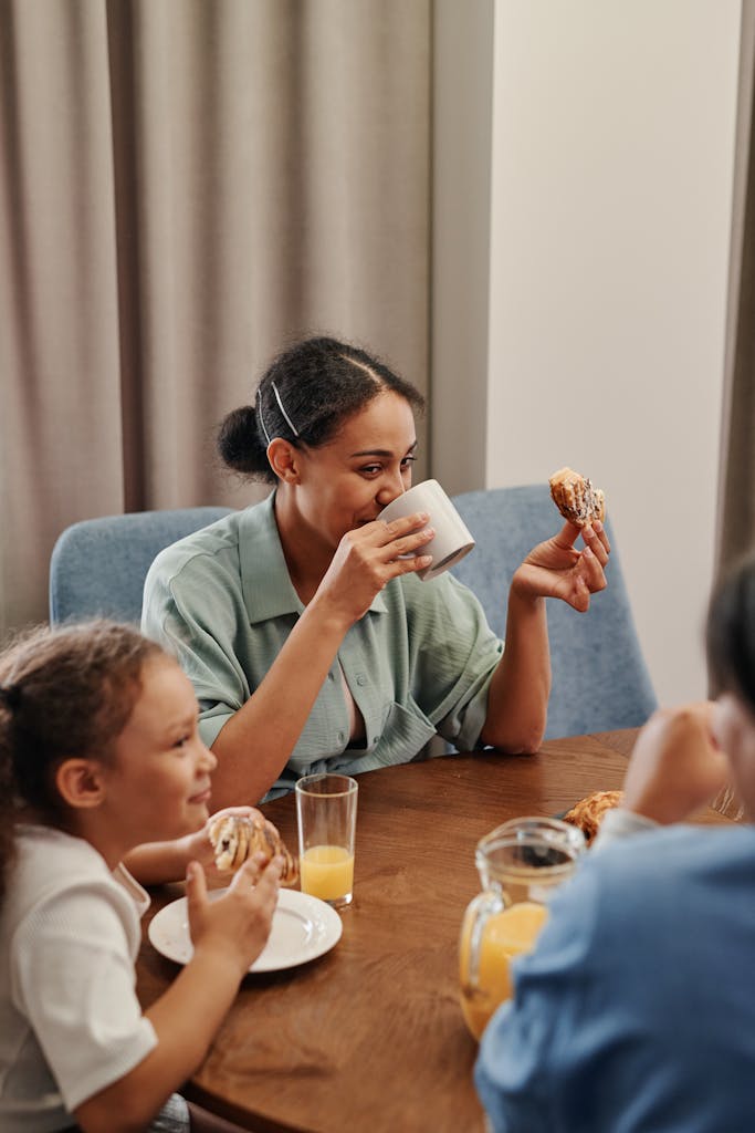 A joyful family breakfast scene featuring a mother and children sharing food and drinks indoors.