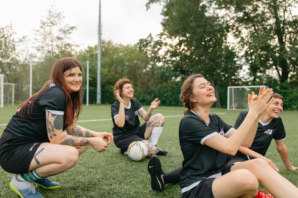 A joyful women's soccer team sitting together, enjoying camaraderie on a sunny day.