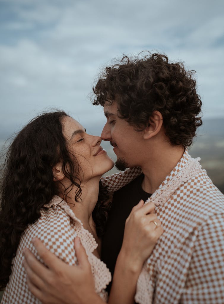 A loving couple embraces outdoors under a cloudy sky, captured in a tender moment.