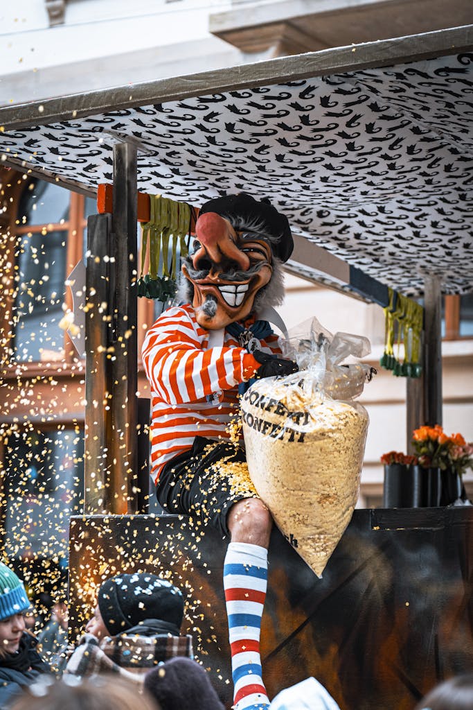 A masked performer sits and throws confetti during a lively street festival.