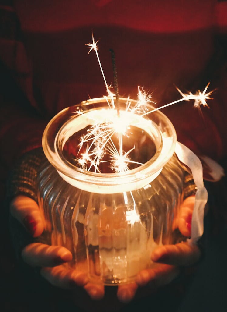 A mesmerizing view of a sparkler glowing inside a glass jar held by hands.