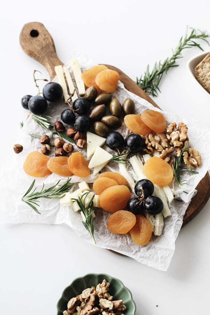 A rustic cheese platter with assorted nuts, dried fruits, and olives on a wooden board.