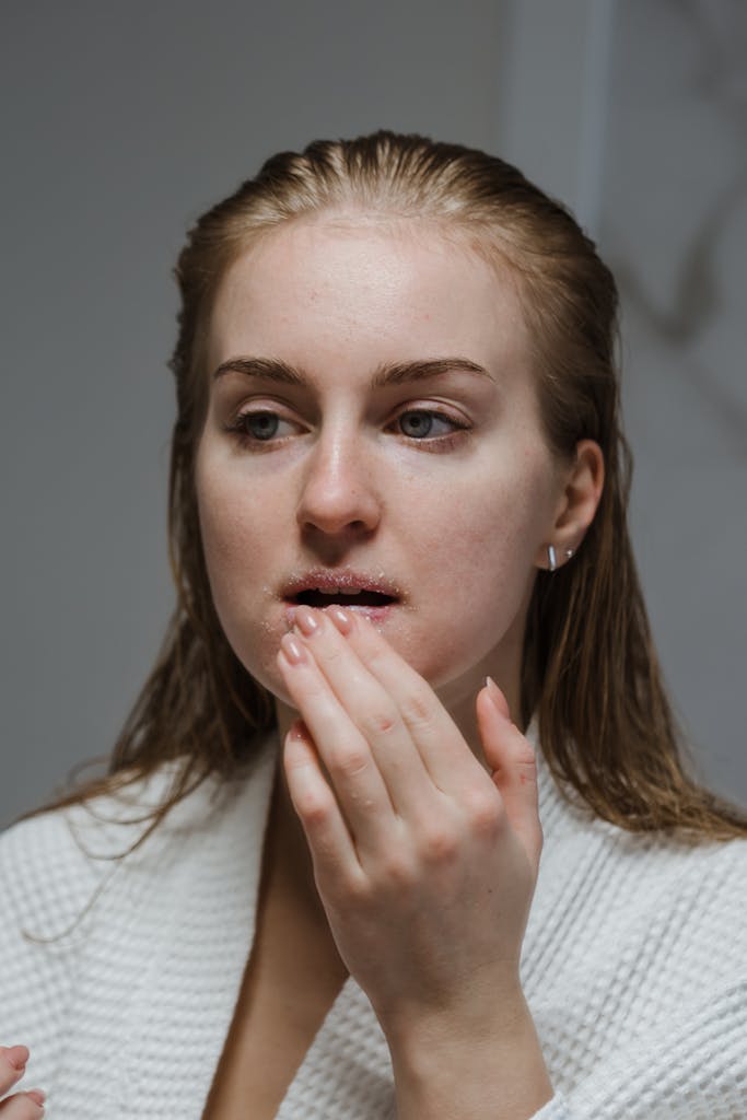 A woman exfoliates her lips as part of a beauty routine indoors, focusing on self-care.