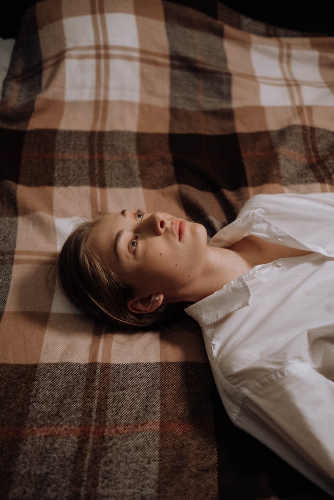 A woman lies on a plaid blanket, appearing deep in thought and solitude.