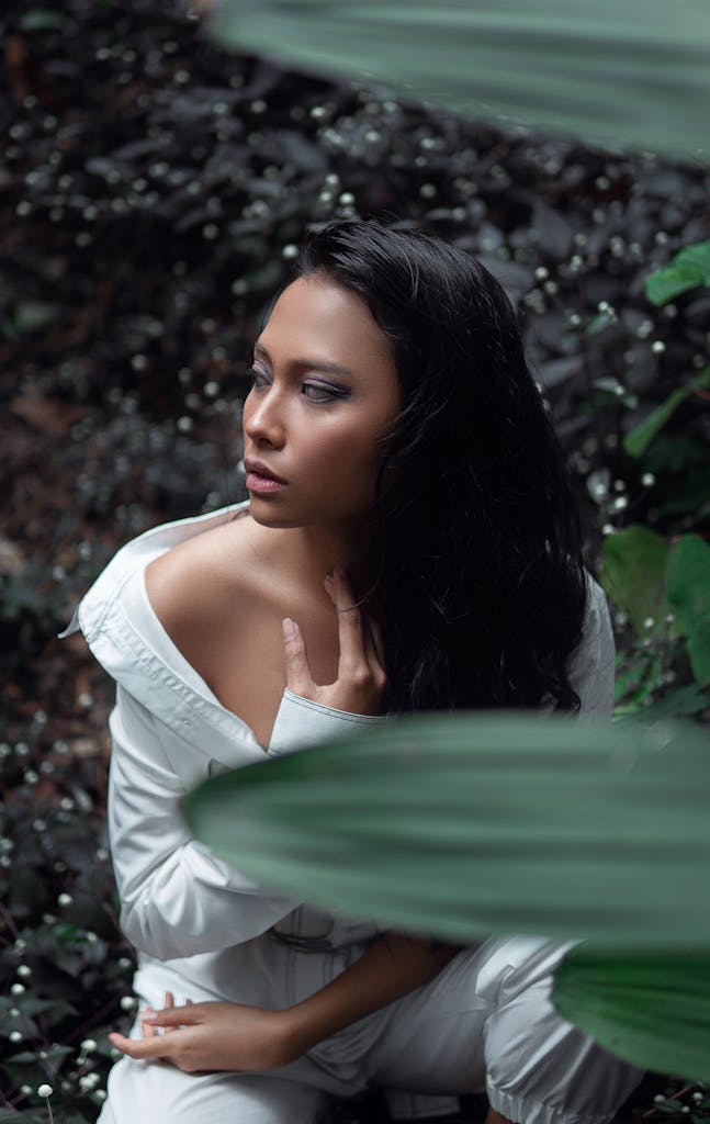 A woman poses gracefully amidst lush foliage outdoors in Bandung, Indonesia.