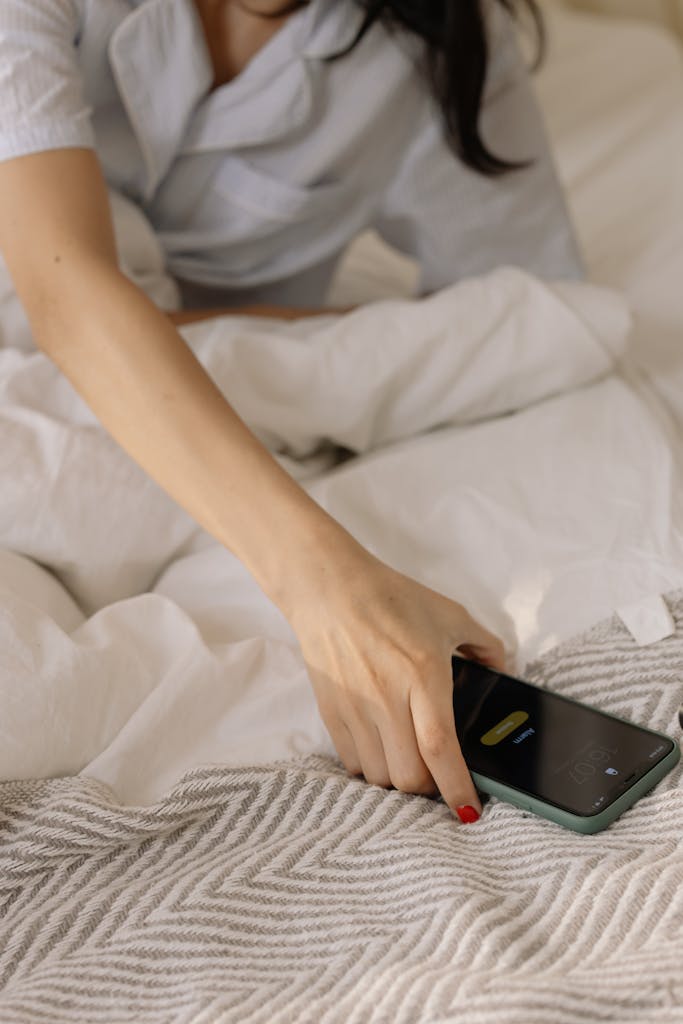 A woman reaches for her smartphone while in bed, starting her day.