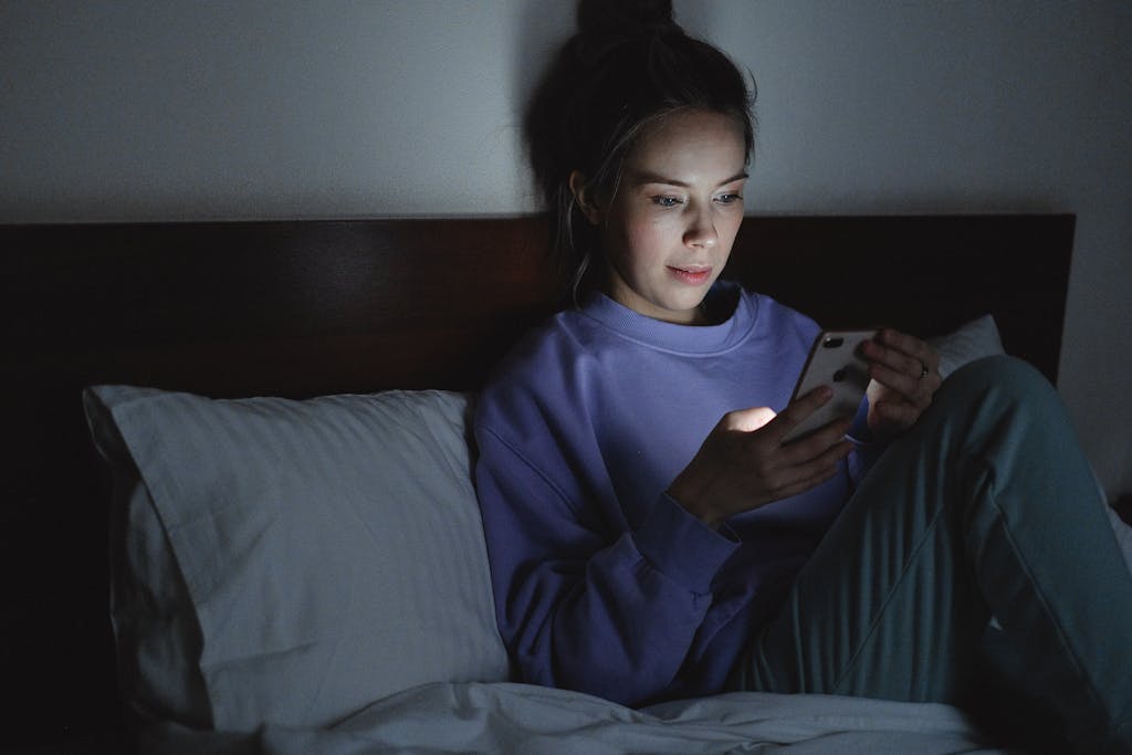 A woman using her smartphone in bed at night, illuminated by the device's light.