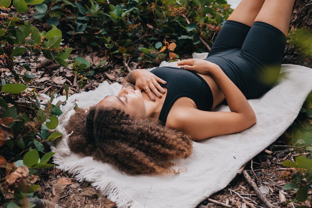 A woman with curly hair lying on a blanket outdoors in activewear, embodying relaxation and connection to nature.