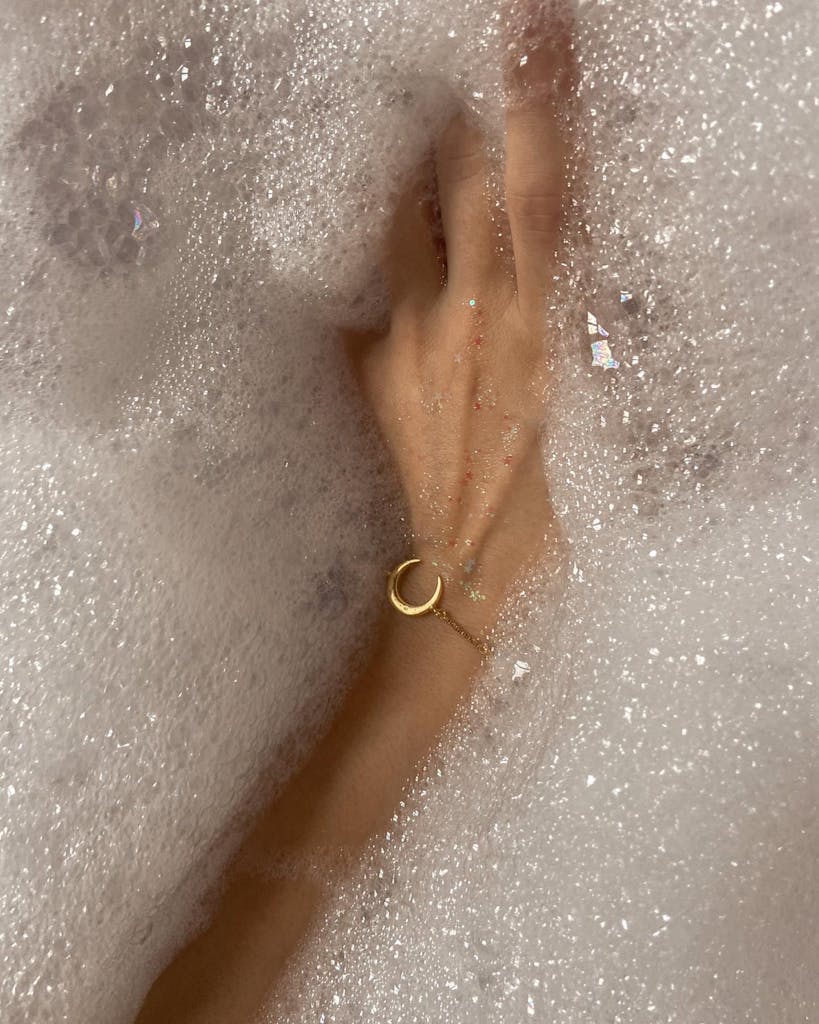 A woman's hand with a bracelet submerged in a bubbly bathtub, capturing serenity and self-care.