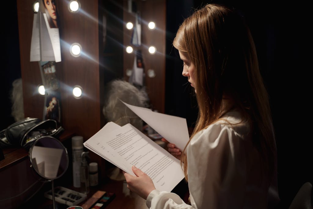 Actress reading script in a dressing room, surrounded by makeup and lights.