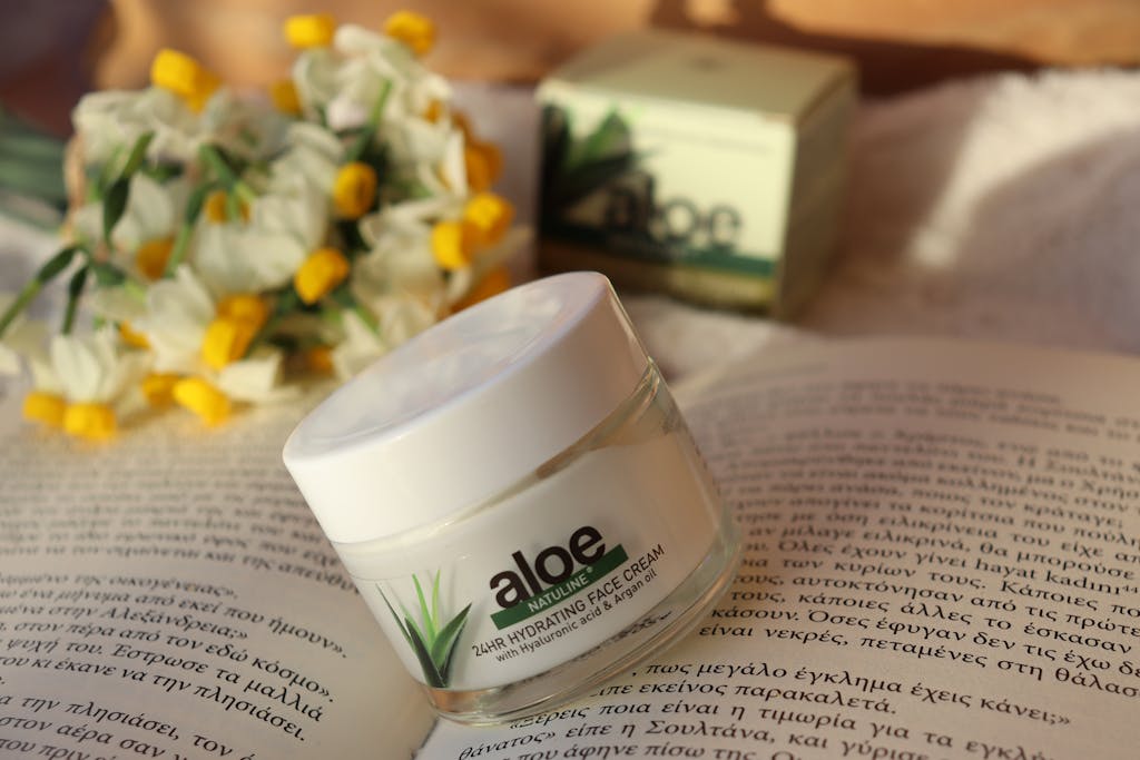 Aloe vera face cream jar on an open book with flowers in a warm setting.
