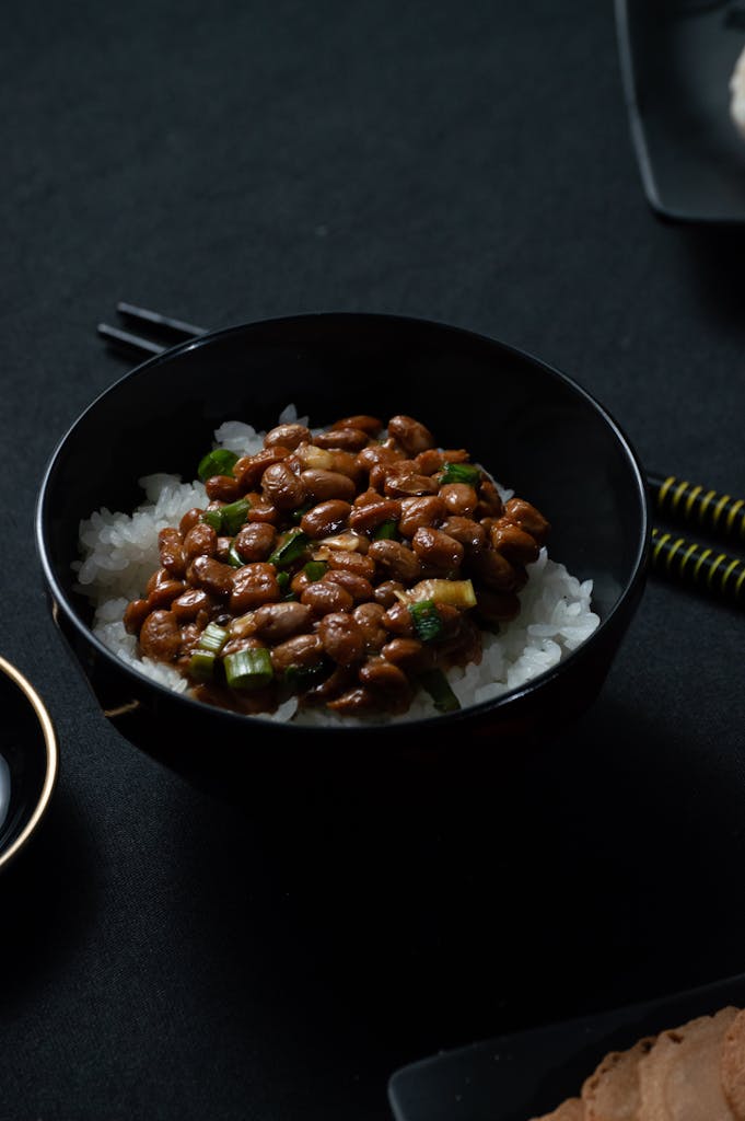 Appetizing natto and rice dish in a black bowl on dark background.