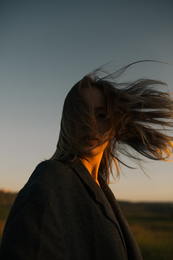 Caucasian woman with long hair in coat at sunset, wind in hair.