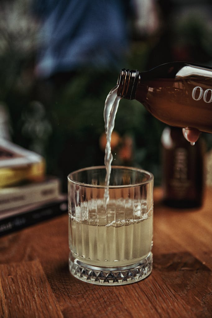 Close-up of kombucha being poured into a crystal glass on a wooden table.