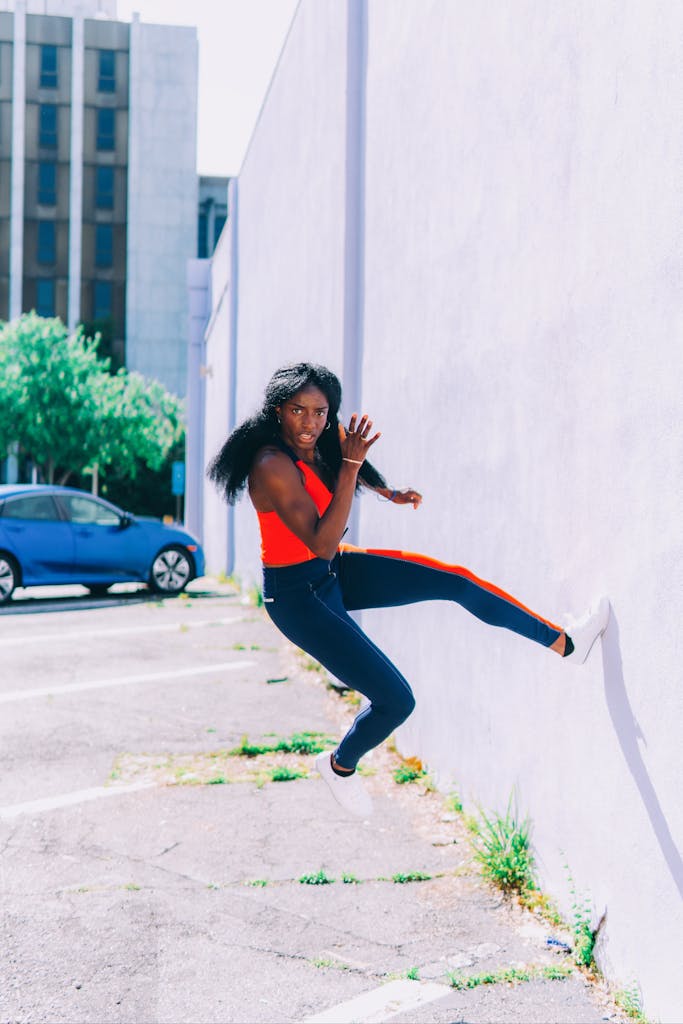 Dynamic shot of a woman in action leaping against a white wall in an urban environment.