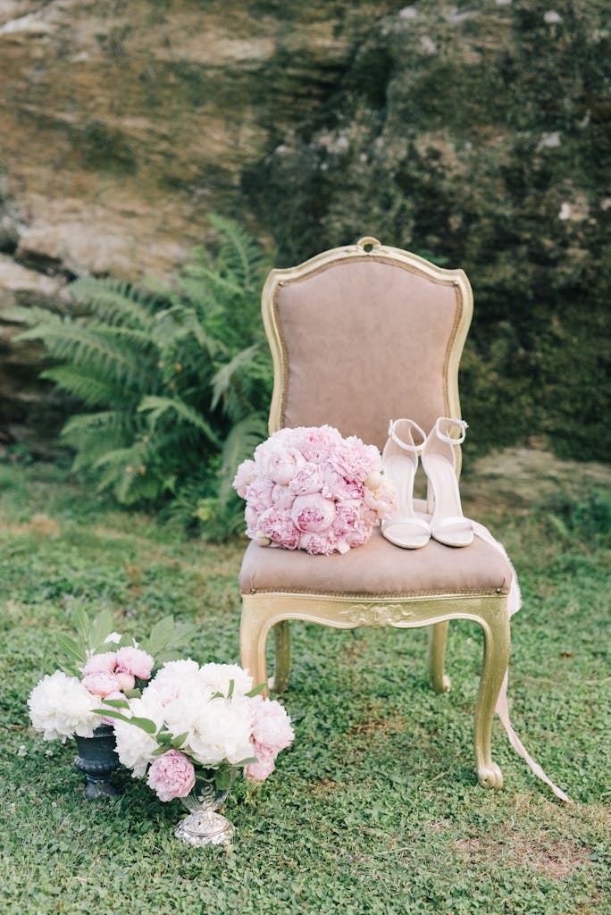 Elegant vintage chair with pink bouquet and high heels in an outdoor garden setting.