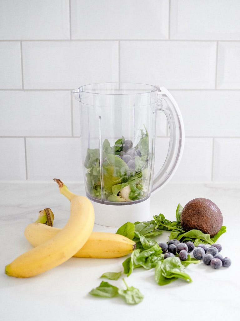 Fresh ingredients for a smoothie including bananas, spinach, and blueberries.