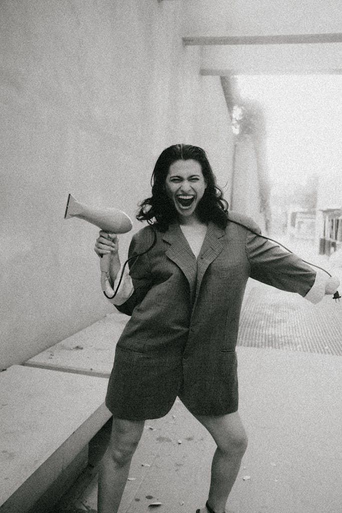 Joyful woman outdoors, energetically posing with a hairdryer, expressing excitement.