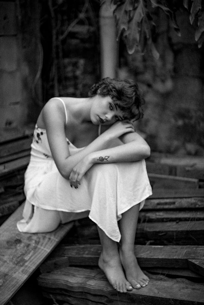 Monochrome portrait of a woman with short hair sitting outdoors, evoking emotion.