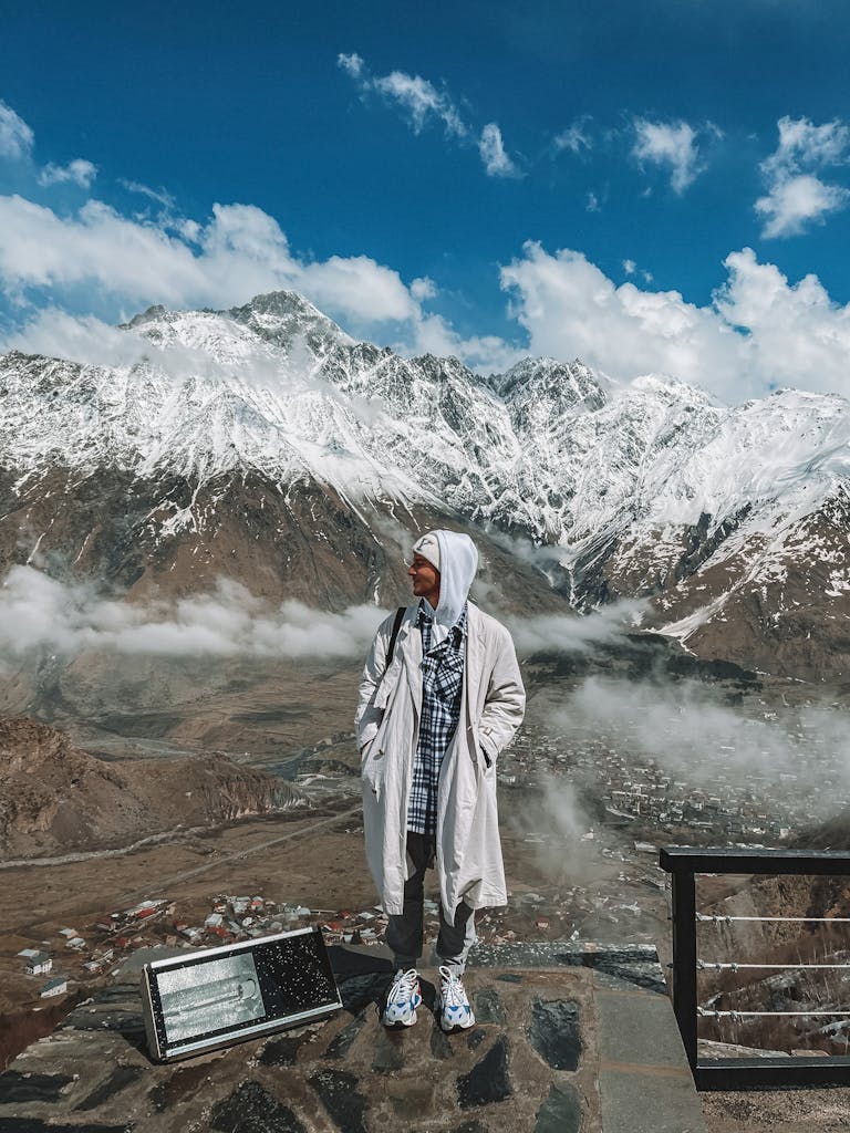 Person standing before a breathtaking snow-covered mountain range with a cloudy sky.