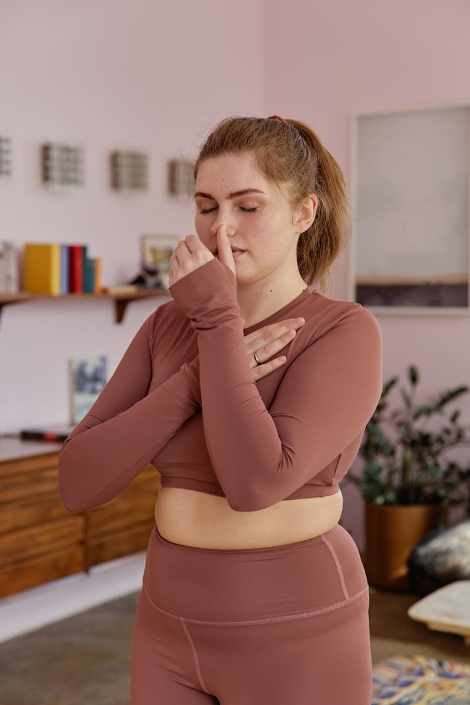 Plus-size woman in activewear performing breathing exercises indoors, promoting wellness and mindfulness.
