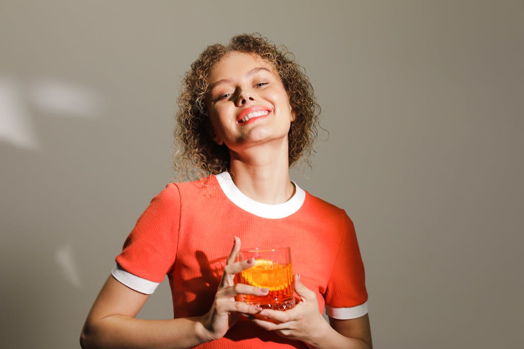 Portrait of a cheerful woman in a studio holding a drink in a glass under warm lighting.