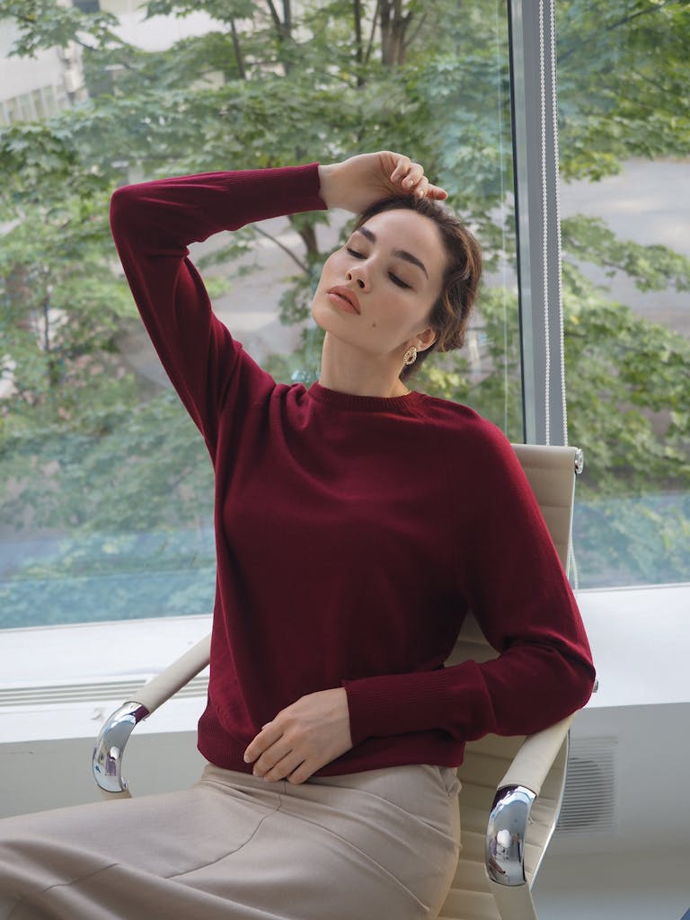 Portrait of a woman in a burgundy sweater, sitting relaxed with eyes closed inside a modern setting.