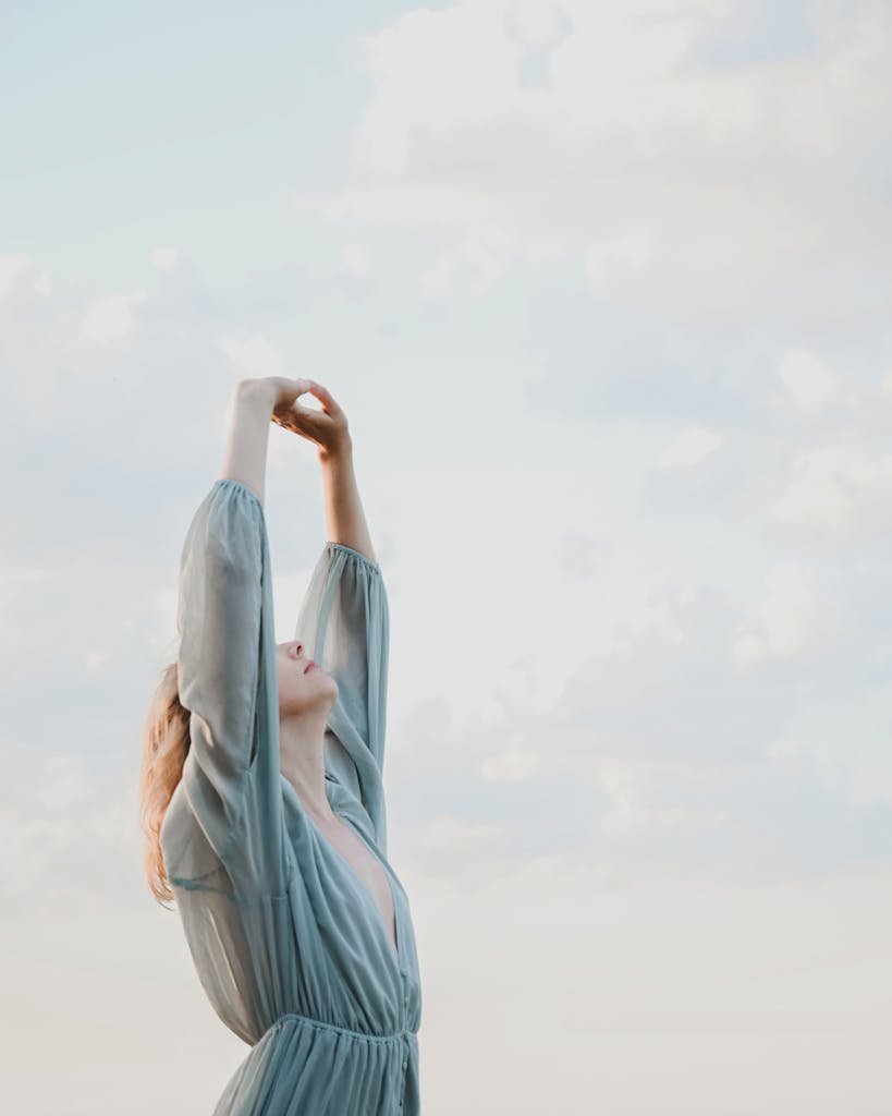 Serene woman enjoying a peaceful moment with raised arms under a cloudy sky.