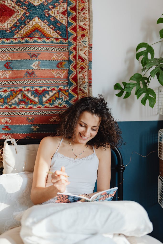 Smiling woman writing in a notebook in a cozy bedroom with sunlight streaming in.