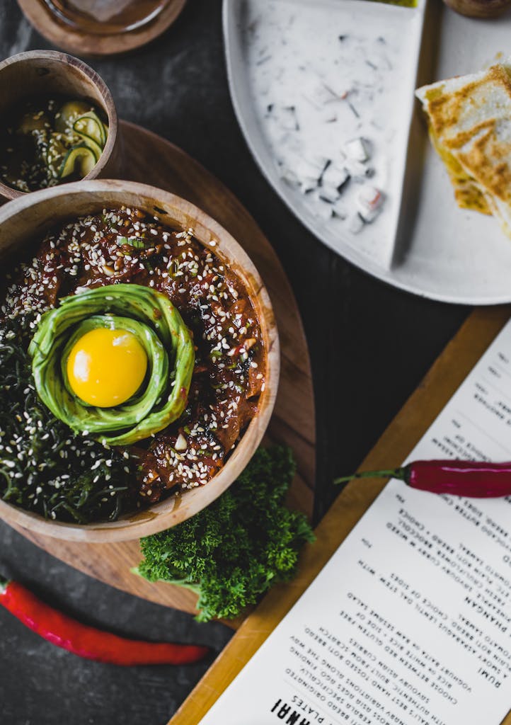Top view of exotic miso bowl with eggplant and avocado served on table near menu and plate of traditional Asian dishes