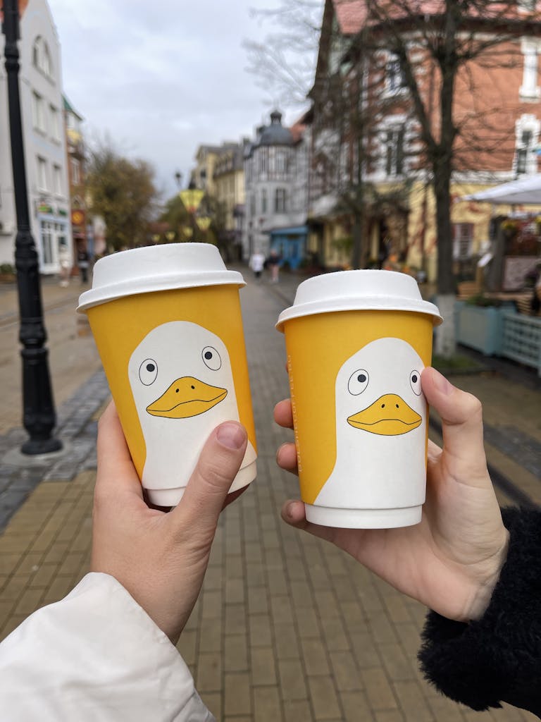 Two hands holding yellow coffee cups with duck design in Zelenogradsk, Russia.