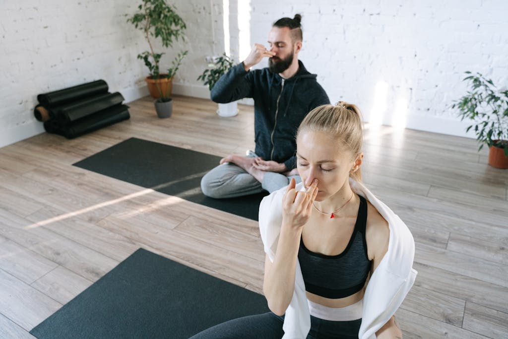 Two individuals practicing yoga breathing exercises indoors, focusing on relaxation.